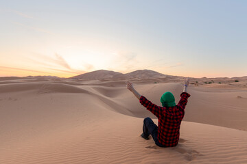 A young man  with open arm sitting on the desert dunes
