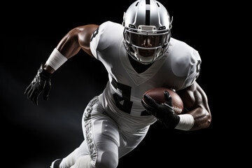 Portrait of American football player running with the ball. Muscular African American athlete in a black and white uniform with an ovoid ball in a dynamic pose. Isolated on black background.