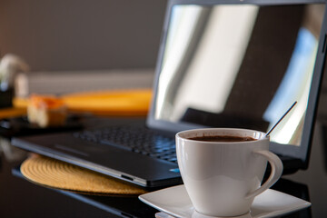 Czarna kawa w białym kubku na tle laptopa - obrazy, fototapety, plakaty