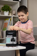 Fototapeta na wymiar A little boy puts a coin into a safe piggy bank. Financial literacy for children.