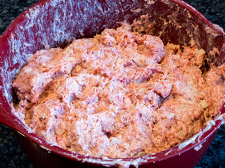 Mixed meatball ingredients, ground meat, onion, breadcrumbs, milk, egg and spices in a red bowl, ready to be rolled.