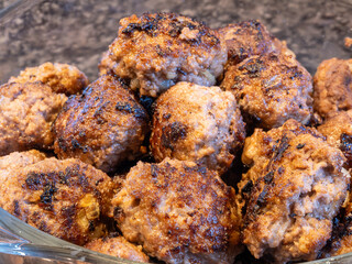 Golden brown meatballs in a glass bowl on a dark granite countertop.