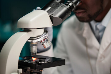 Closeup of microscope with particle of meat under lens, black scientist analyzing it