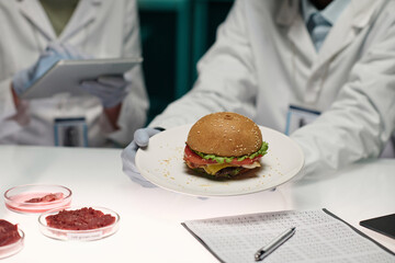 Unrecognizable lab worker holding plate with artificial meat hamburger