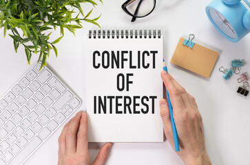 Conflict of interest text on blank business card being held by a woman's hand with blurred background. Business concept about conflict of interest.
