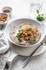 Thick lentil soup with croutons and meat chips served for dinner on white background