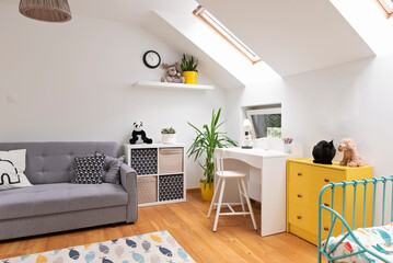 Room child in the attic with window, carpet in modern design on the wooden floor, white wall and yellow furniture. Cozy interior for teenager with desk, bed and sofa.	