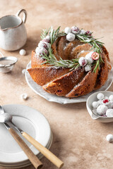 Christmas bundt cake decorated with glaze, cranberries and rosemary served on beige table. Homemade cake recipe