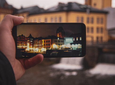 Cropped hand holding a mobile phone against building