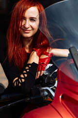 Fototapeta na wymiar Red-Haired Woman Posing on a Motorcycle. A woman with red hair sitting on a motorcycle