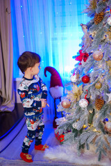 Little Boy Excitedly Admiring the Beautifully Decorated Christmas Tree. A little boy standing in...