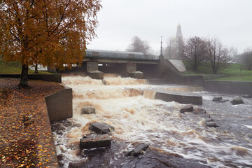 Waterfall of an old dam and fog and the Orthodox Church, autumn trees in the suburbs of St....