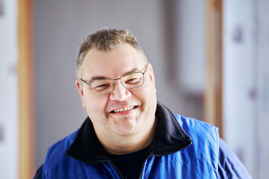 Large build man smiles cheekily, his face in glasses close-up