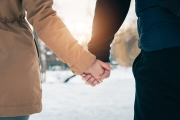 Unrecognizable couple standing side by side holding hands outdoors at sunset in winter.