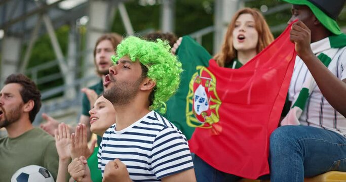 Football fans watching tournament at stadium. Young multinational people cheering for Portugal team while holding national team flag. Crowd shouting congratulation for winners.