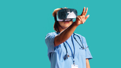 Healthcare professional wearing virtual reality headset remotely checking patient. Nurse isolated over blue studio background using high-tech advanced clinical vr gadget, close up