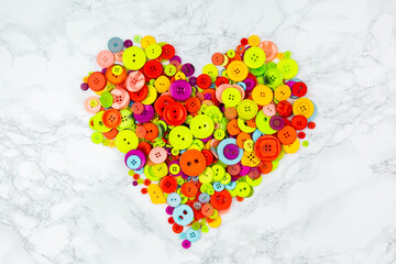 Heart-shaped pile of buttons on white background. Multicolored clothes-buttons shaped like a heart. Bright buttons for needlework isolated on white background. Love Sewing, tailoring. 