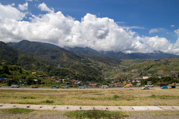 A scenic view of a valley with a small town nestled among lush green mountains under a dynamic cloudy sky.