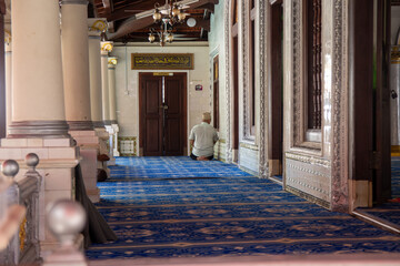 A person in solitary prayer in a peaceful mosque interior with ornate decor. - obrazy, fototapety, plakaty
