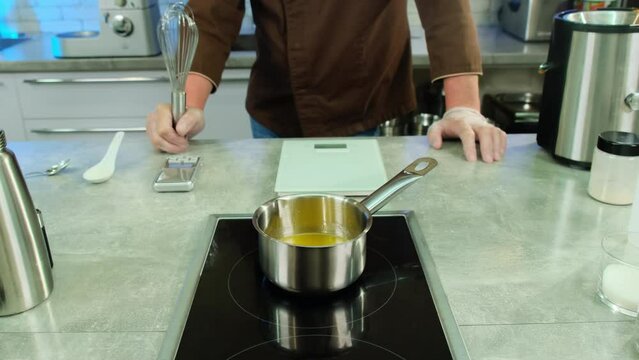 Professional cook places saucepan on hot stove to warm sauce. Male culinarian choose correct mode on stove to warm sauce