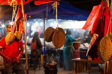 Durian fruit hanging at a vibrant night market with bustling activity