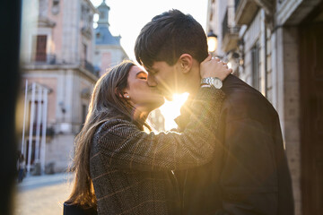 two lovers kissing in the street at sunset. young couple spending valentine's day as a couple. - obrazy, fototapety, plakaty