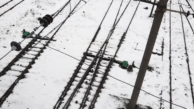 aerial view of railway tracks during winter, with snow covering the ground. Multiple tracks intersect and diverge, indicating a switching area for trains. 