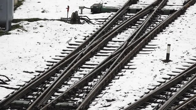 The converging lines of multiple tracks create a sense of depth and perspective, and there are snow patches interspersed between the wooden sleepers and the rails.