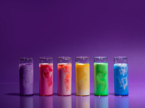 Row of six multi coloured glass vials filled with milk and LED lights against a purple background
