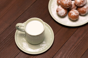 Top View Cup Of Milk, Zeppole Or Paczki On Plate With Powdered Sugar On Wooden Table. Fat Thursday Carnival or Tlusty Czwartek, Christian tradition. Doughnut, Delicious Donuts. Horizontal Plane