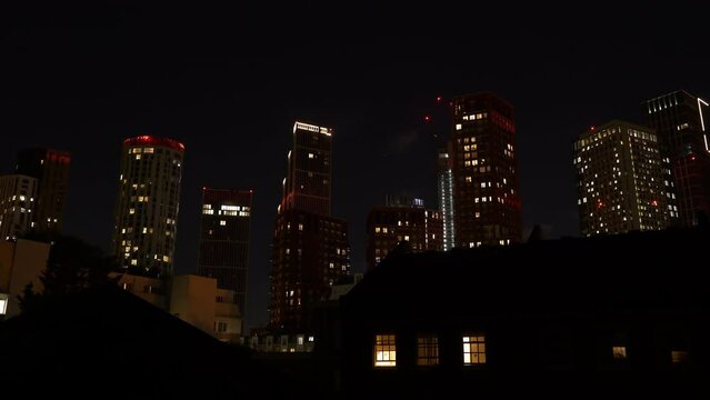TIME LAPSE: Glowing window lights of tall city skyscrapers under dark night sky. Magnificent urban landscape with modern commercial and residential buildings in the London district at night time.