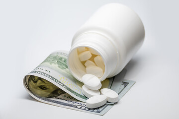 Concept of the cost of medicine, represented with a bottle of pills on a hundred dollar bill.