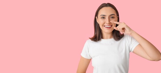 Young woman pointing at her nose on pink background with space for text