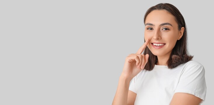 Young woman pointing at her nose on grey background with space for text