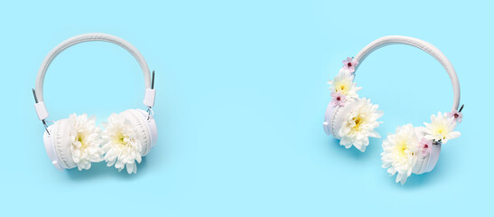 Modern wireless headphones and beautiful chrysanthemum flowers on blue background with space for text