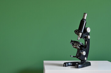 Vintage microscope on table near green wall