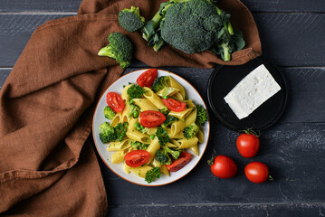 Plate with tasty penne pasta and vegetables on dark wooden background