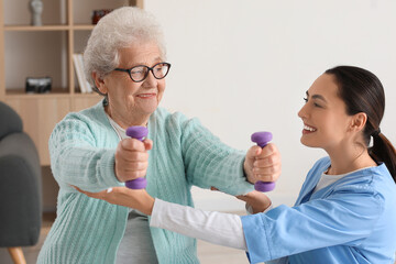 Young caregiver and senior woman training with dumbbells at home