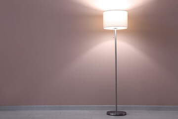 Glowing floor lamp near beige wall in dark room
