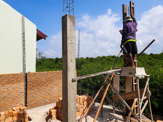 Portrait of a house being built and a builder standing near the pillar