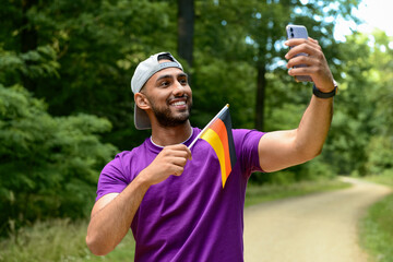 Young man with flag of Germany taking selfie in forest