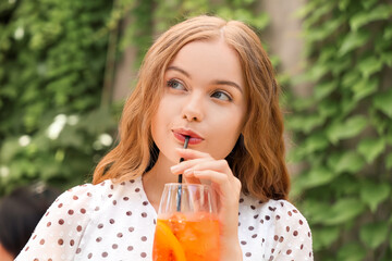 Beautiful young woman drinking tasty aperol spritz cocktail in cafe, outdoors