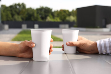 Coffee to go. Couple with paper cups at table outdoors, selective focus