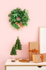White chest of drawers with Christmas decorations and gift boxes near pink wall