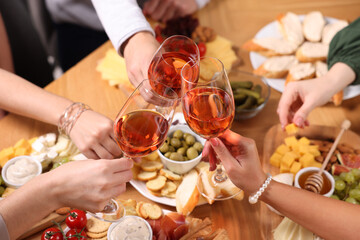People clinking glasses with rose wine at wooden table, above view