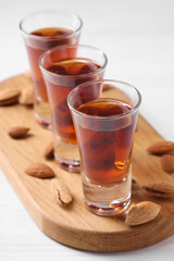 Shot glasses with tasty amaretto liqueur and almonds on white wooden table, closeup