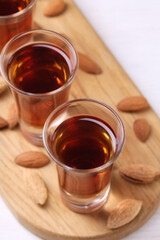 Shot glasses with tasty amaretto liqueur and almonds on white wooden table, closeup