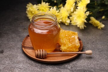 Sweet golden honey in jar, dipper and honeycomb on grey textured table