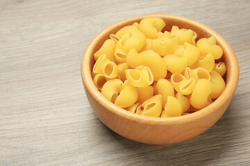 Raw macaroni pasta in bowl on light grey wooden table, closeup. Space for text