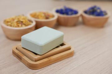 Soap bar and bowls of dry flowers on light wooden table, space for text. Spa therapy